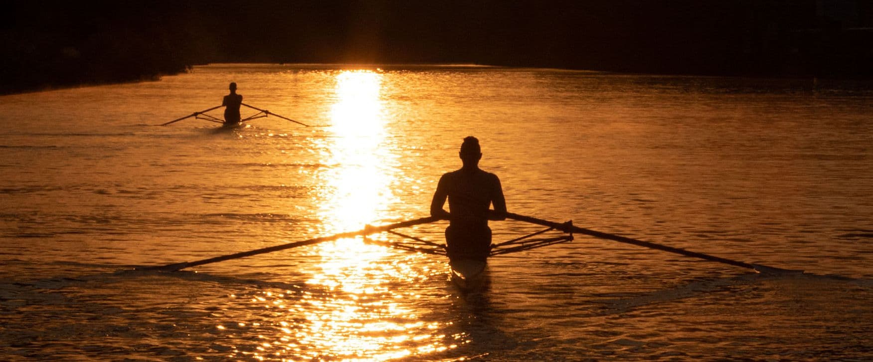 two people are rowing a boat on a lake at sunset .