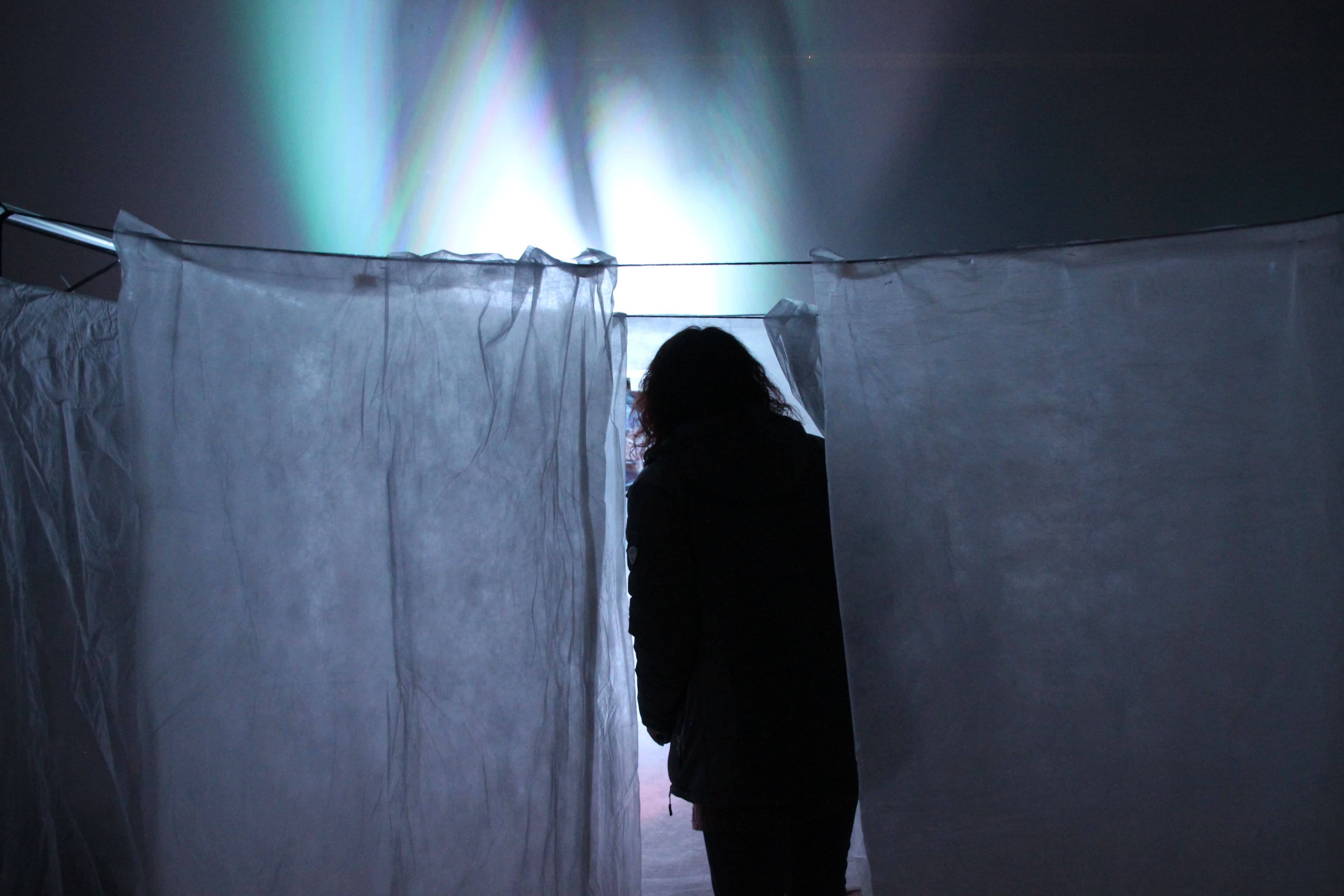 a woman is standing in a dark room behind a white curtain .