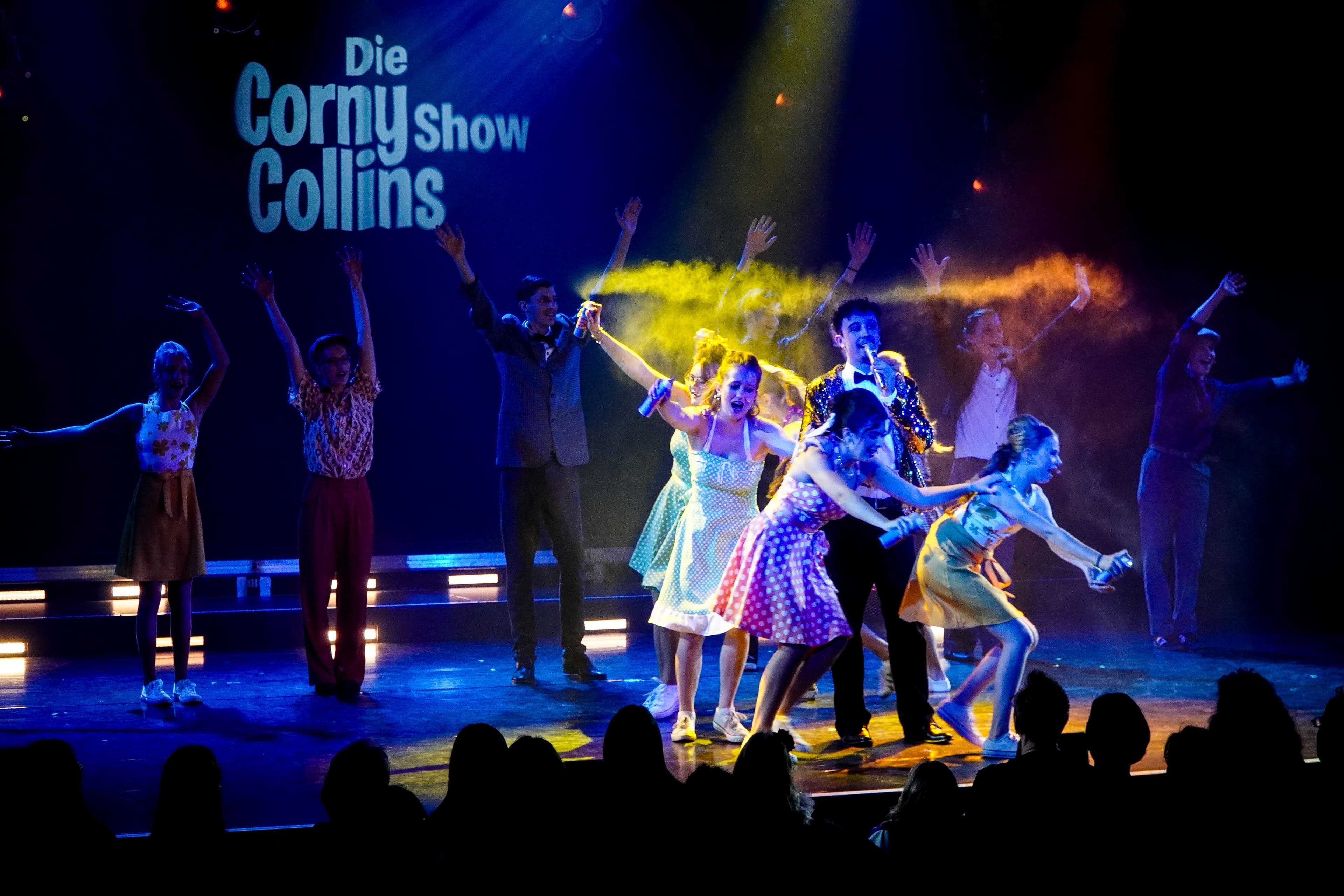 Tänzerinnen mit Sprühflaschen lauen um einen Mann herum.