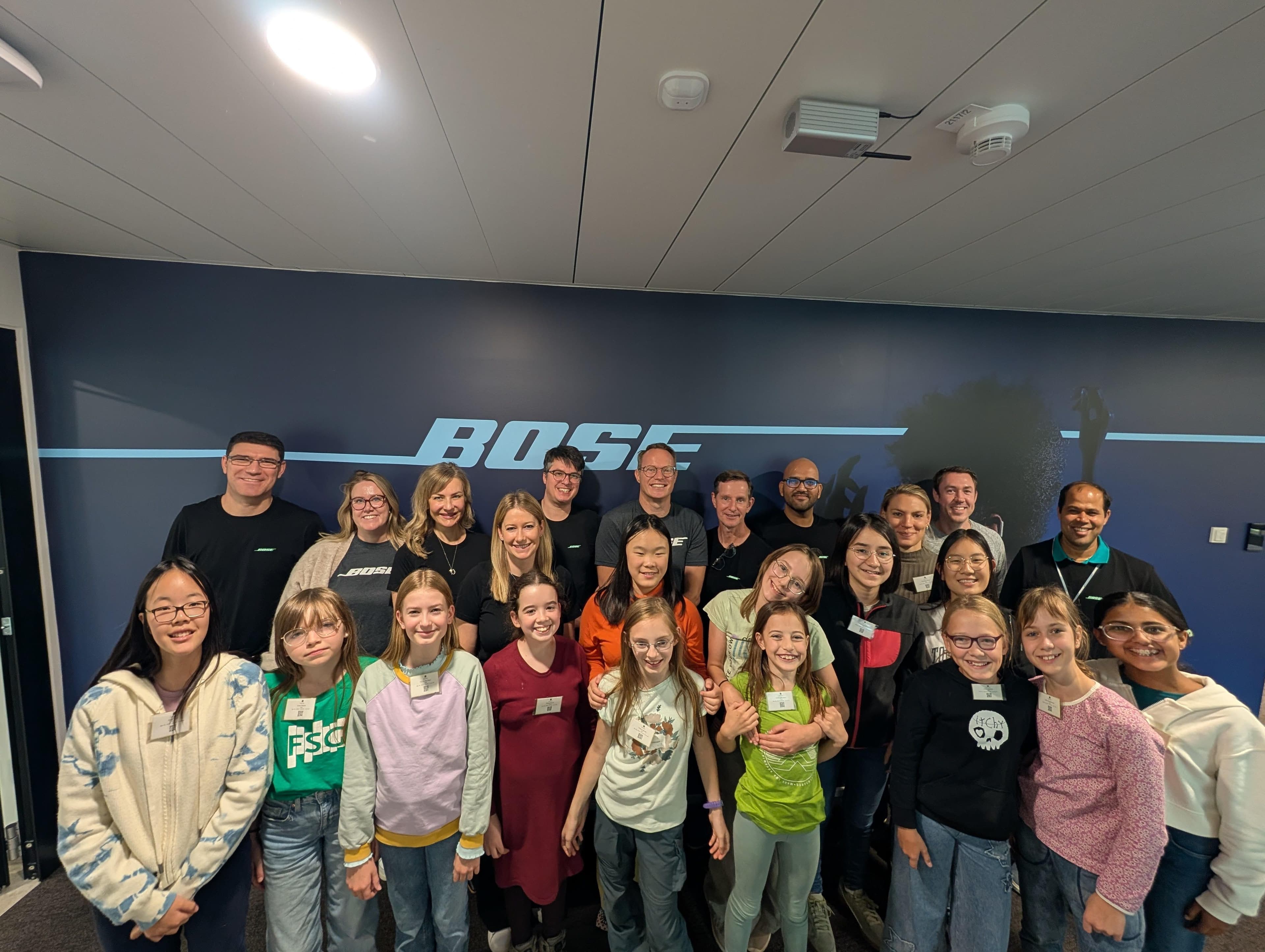 A group of smiling adults and children posing in front of a large Bose logo.