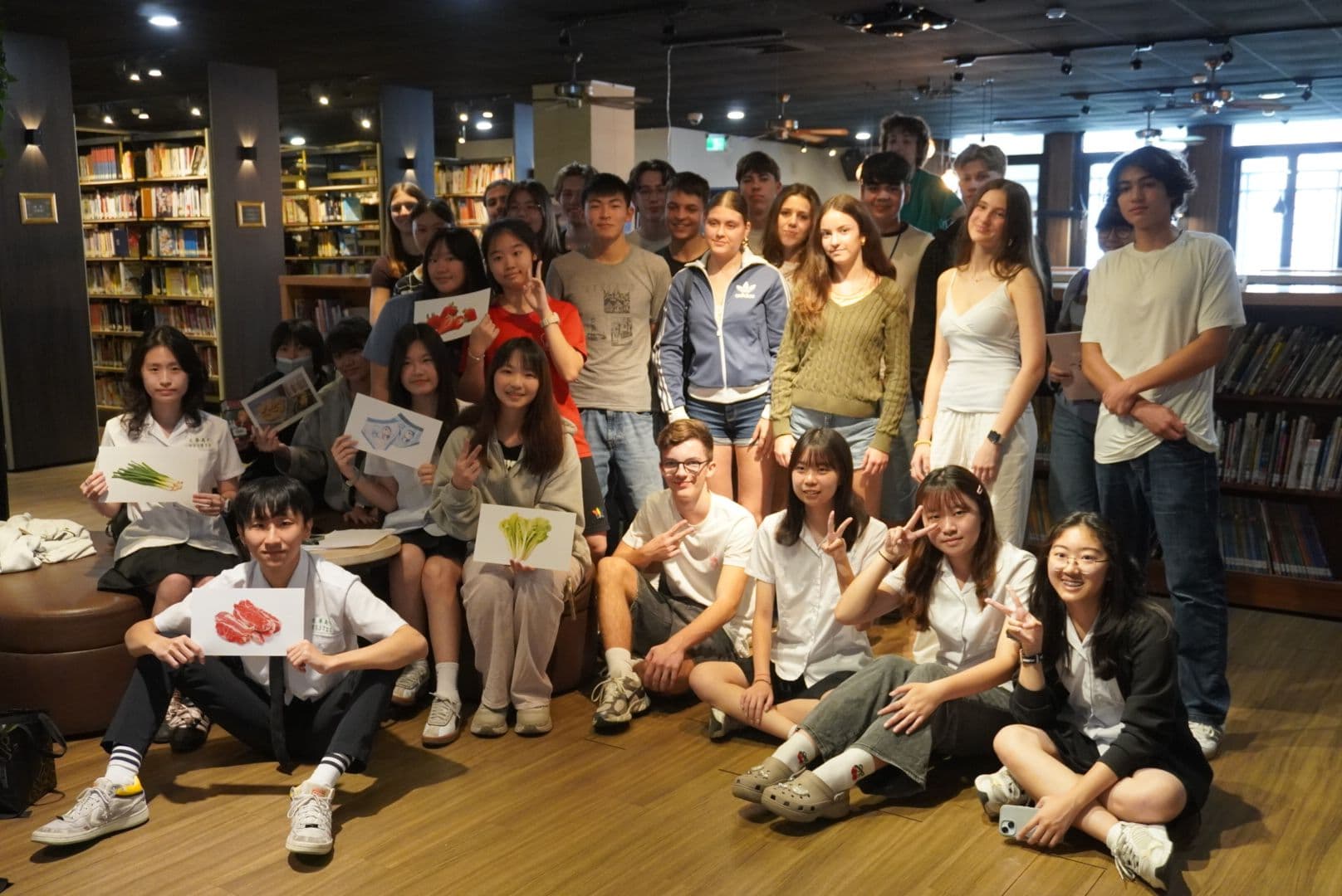 Group of young people in a library, some holding drawings of food and making peace signs.