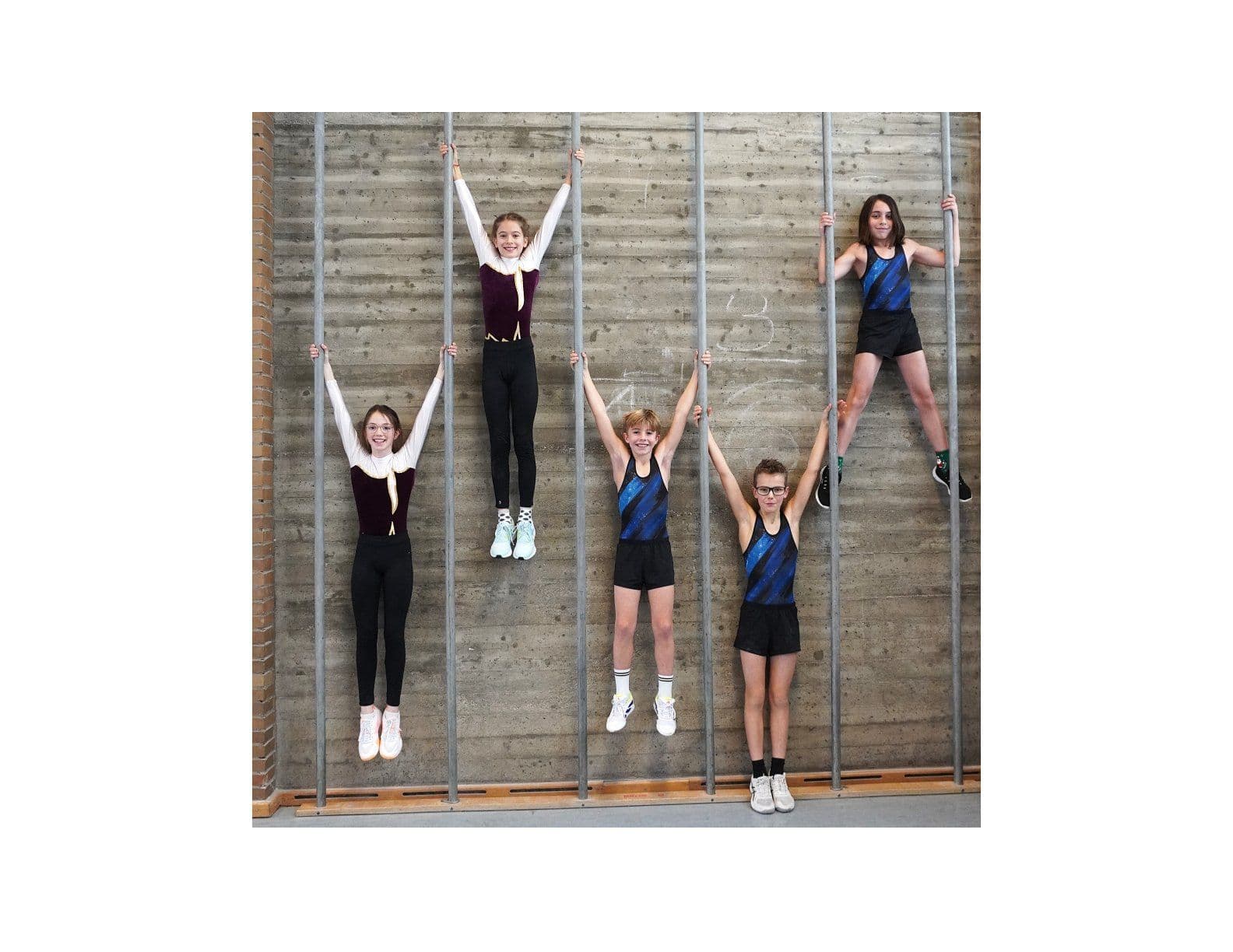 Five young gymnasts hanging and climbing on vertical wall bars.