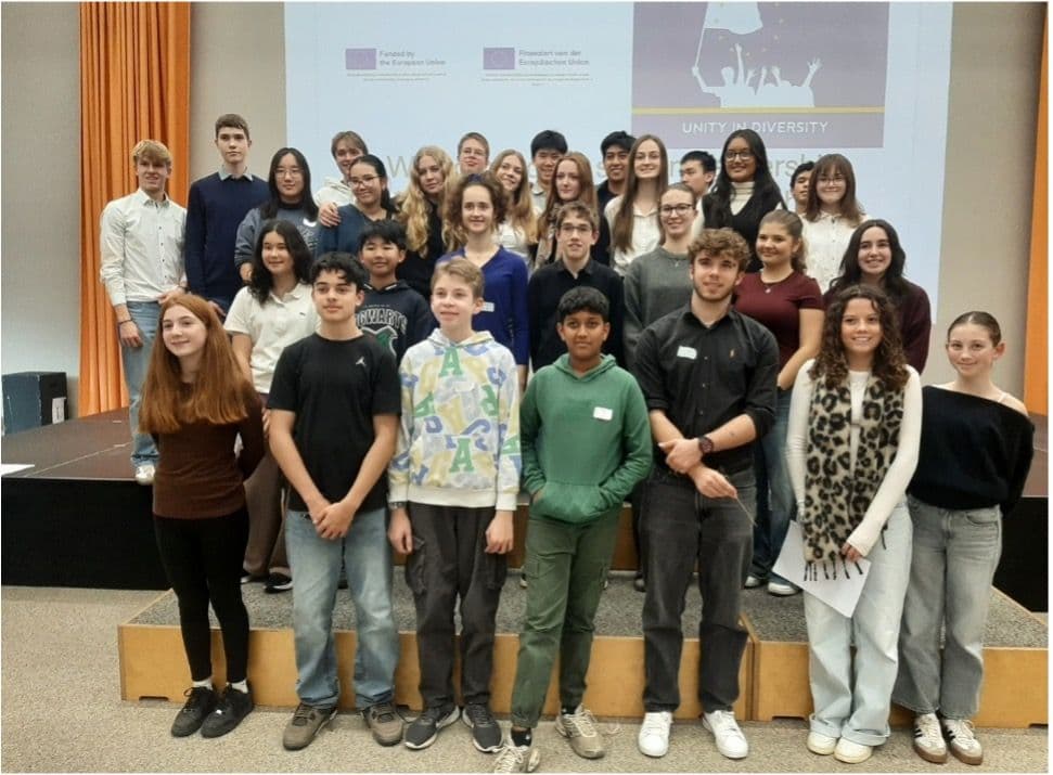 A diverse group of young people posing in front of a screen displaying "Unity in Diversity" and EU logos.