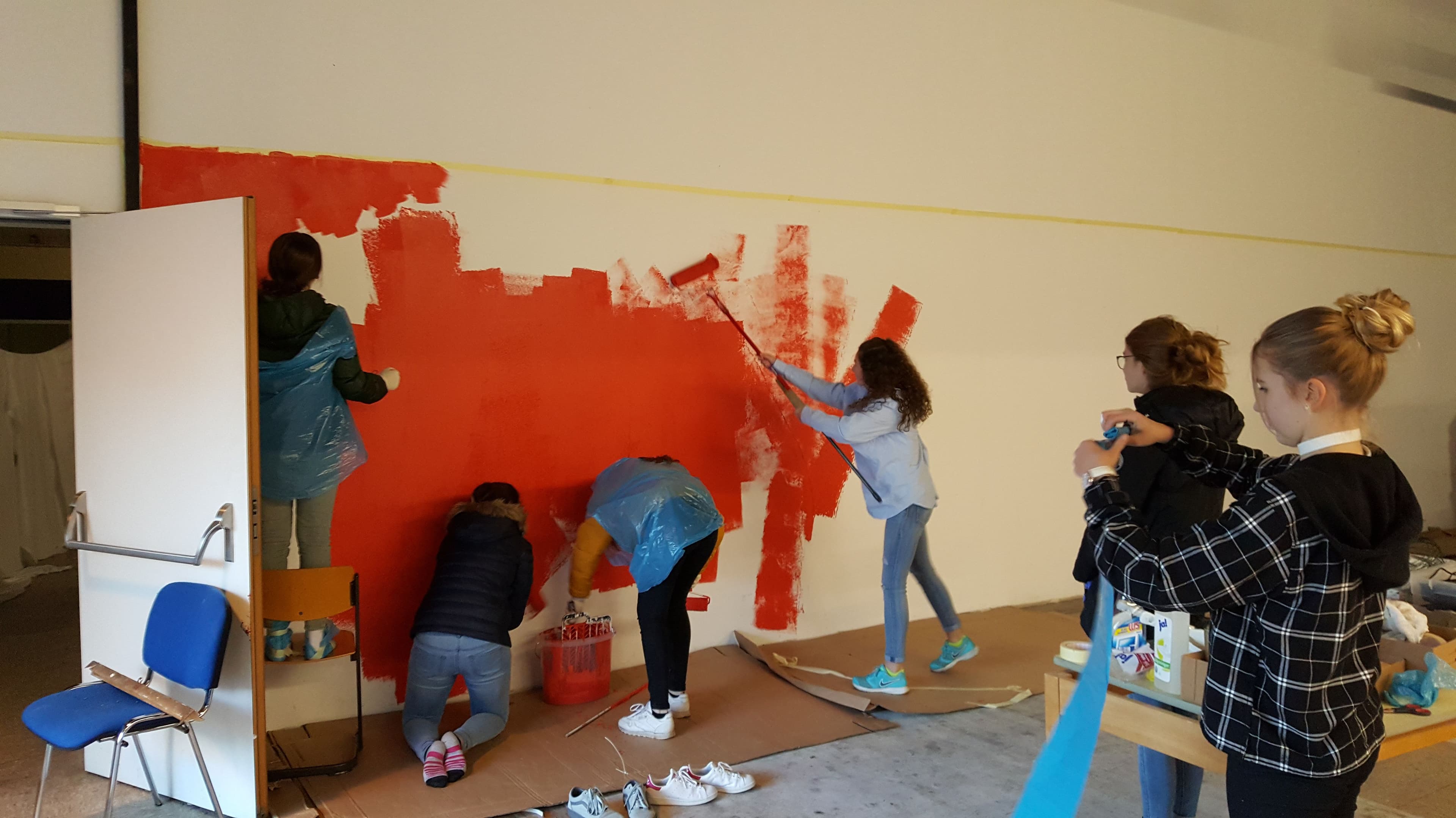 a group of children are painting a wall red .
