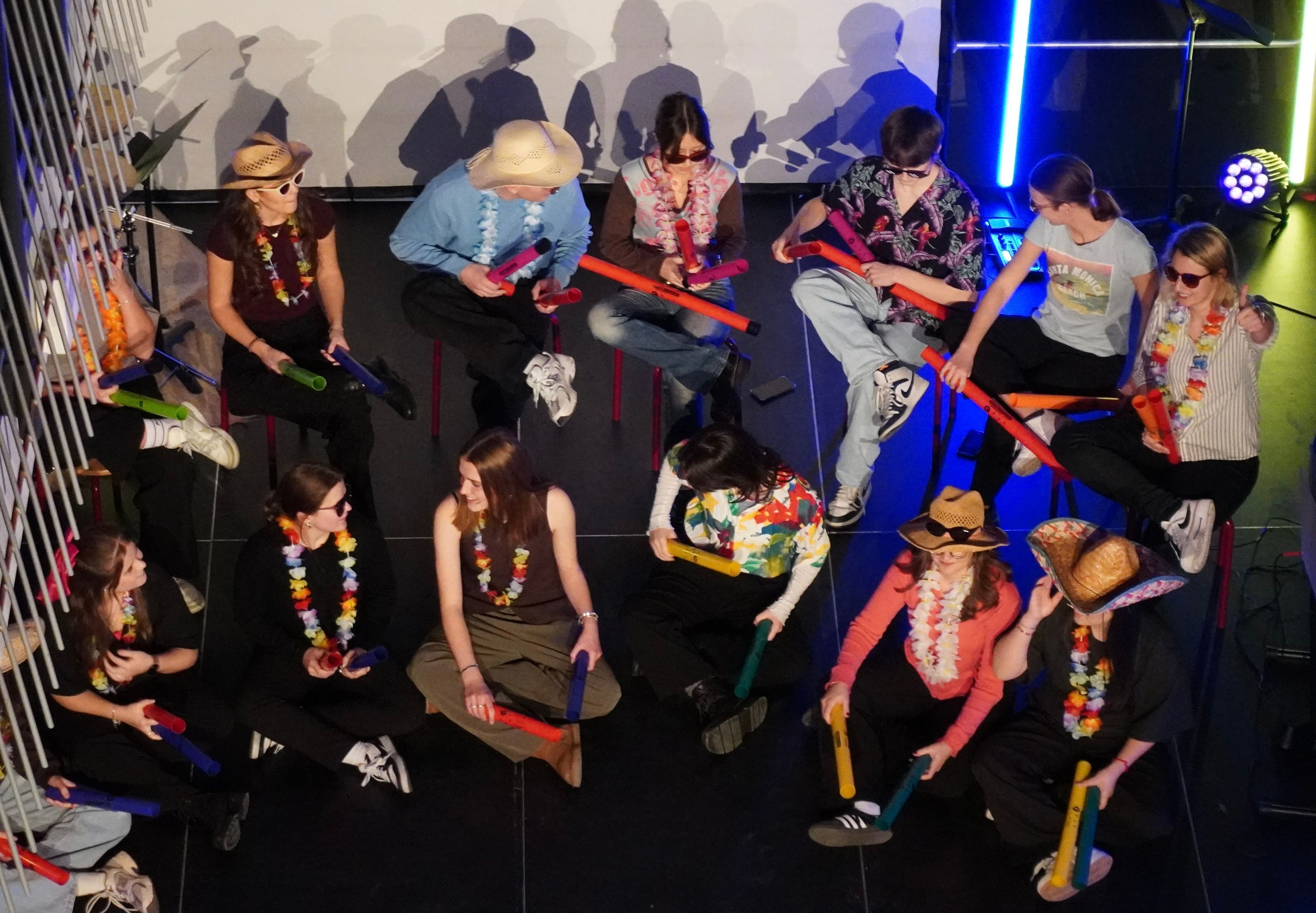 A group of young people, some in hats and leis, playing colorful musical tubes.