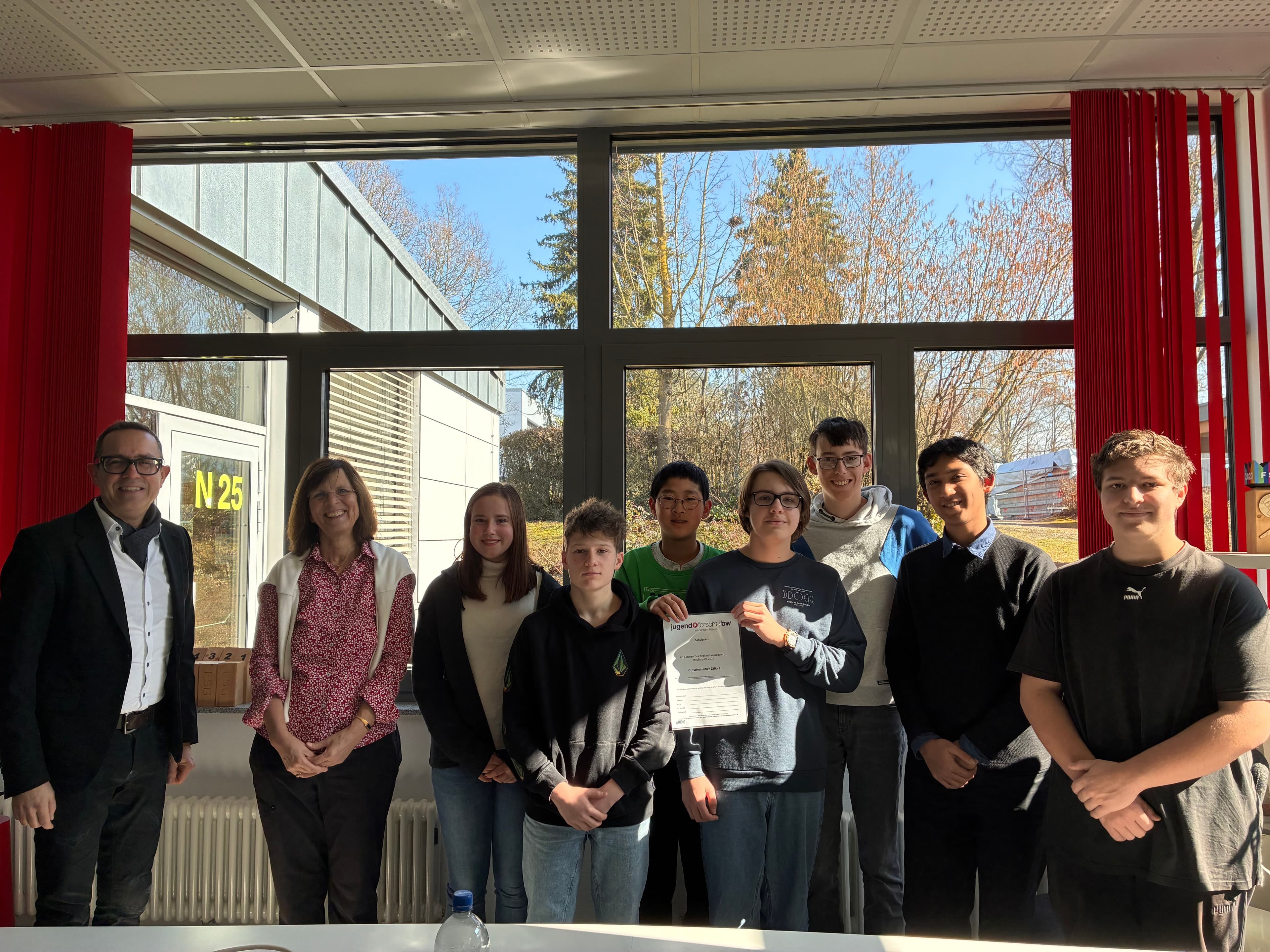 A group of students and two adults pose in a classroom, one student holding a certificate.