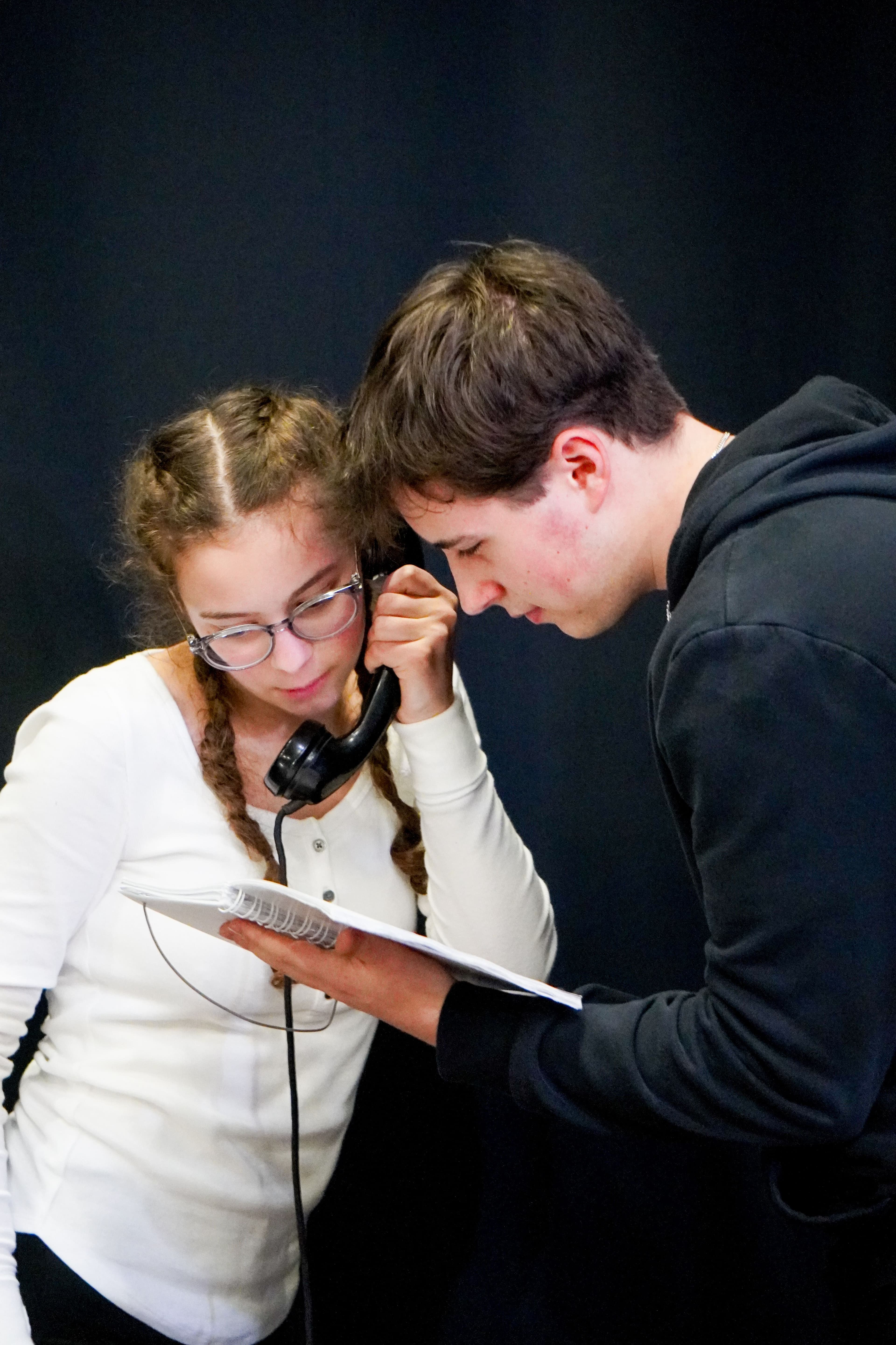 Ein Mädchen hält einen alten Telefonhörer in der Hand, ein Junge schaut in ein Buch während einer Theaterprobe.