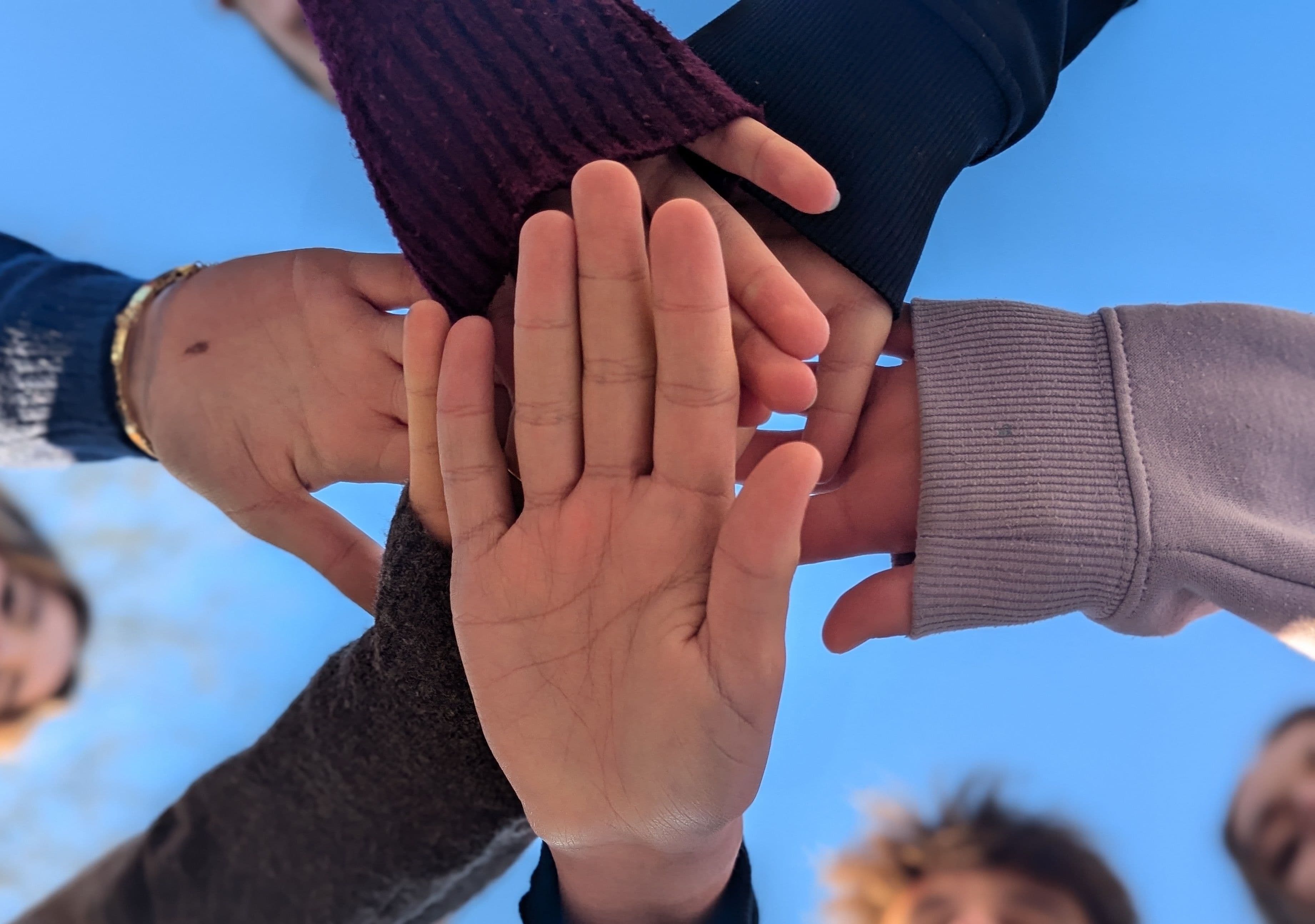 A group of hands stacked together against a blue sky.