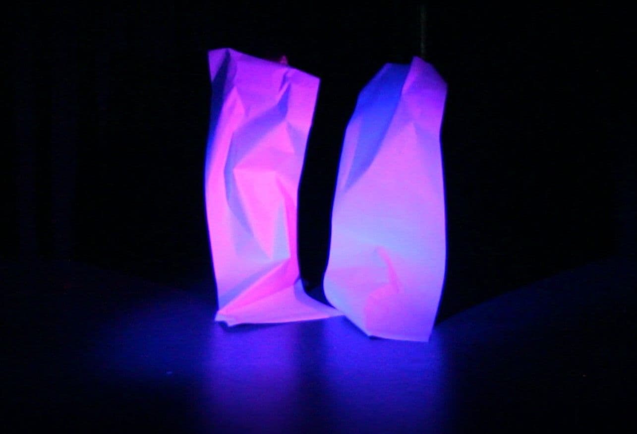 Zei Papierfiguren , violett beleuchtet auf einer schwarzen Bühne