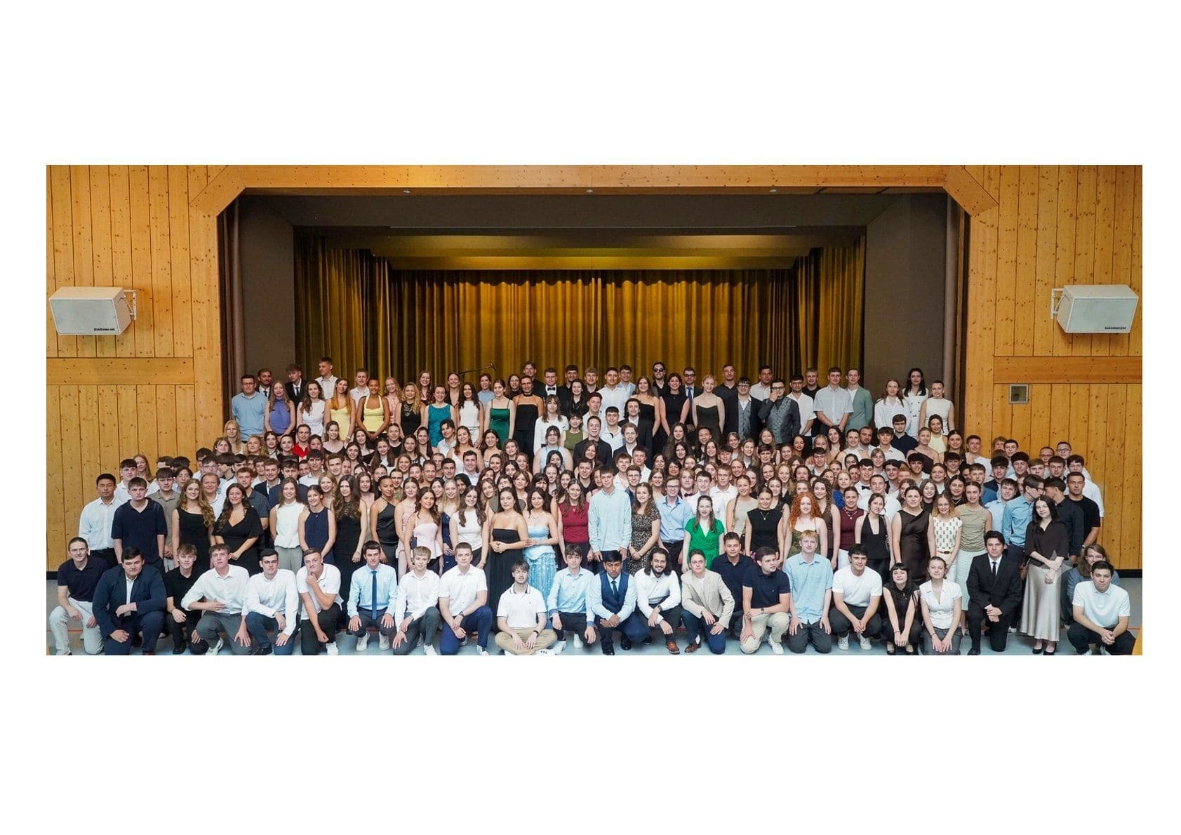 Hundreds of formally dressed young adults pose for a group photo in a hall.