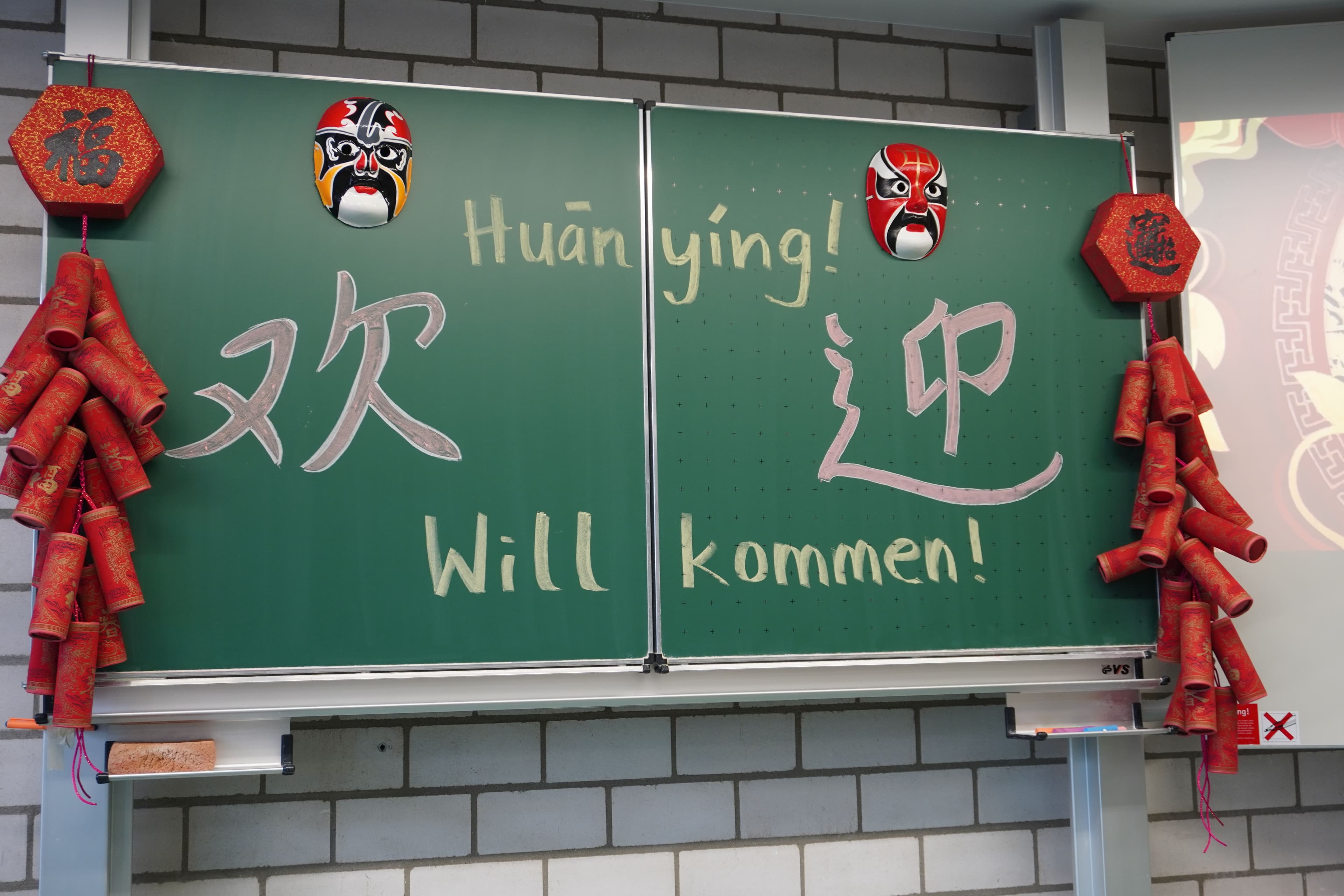 Schriftzug "Willkommen" auf Chinesisch auf einer Schultafel mit chinesischer Deko.