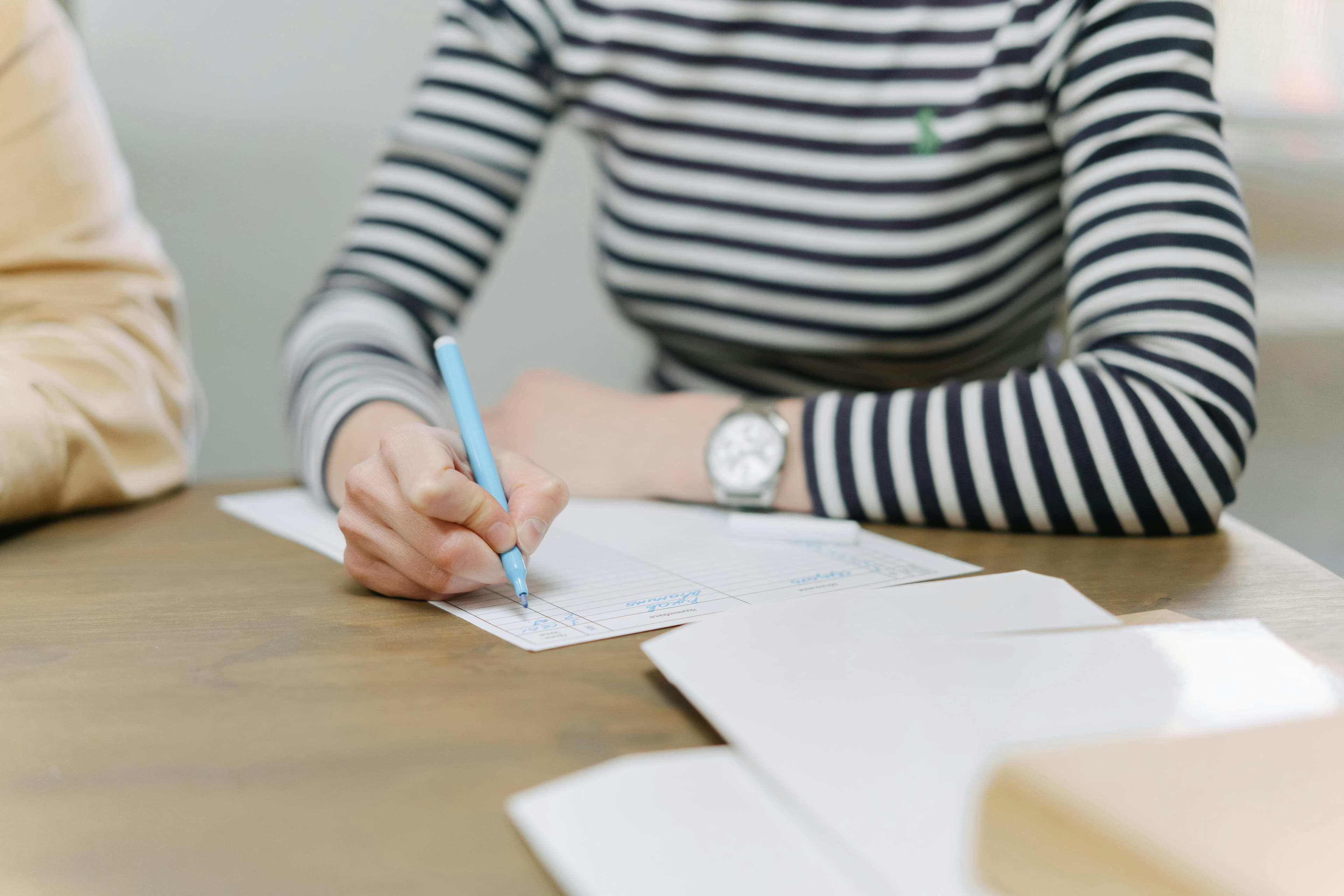 a woman is sitting at a table writing on a piece of paper with a pen .