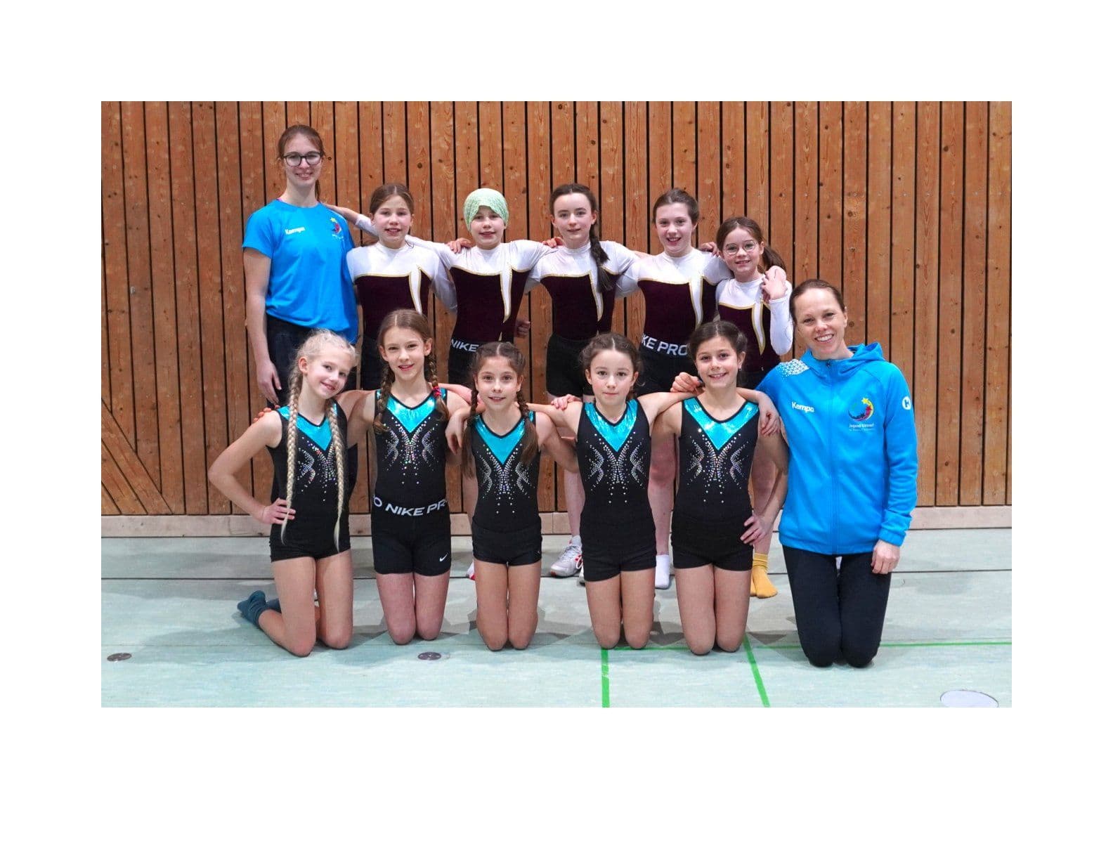 A gymnastics team and two coaches pose for a photo in a gym.