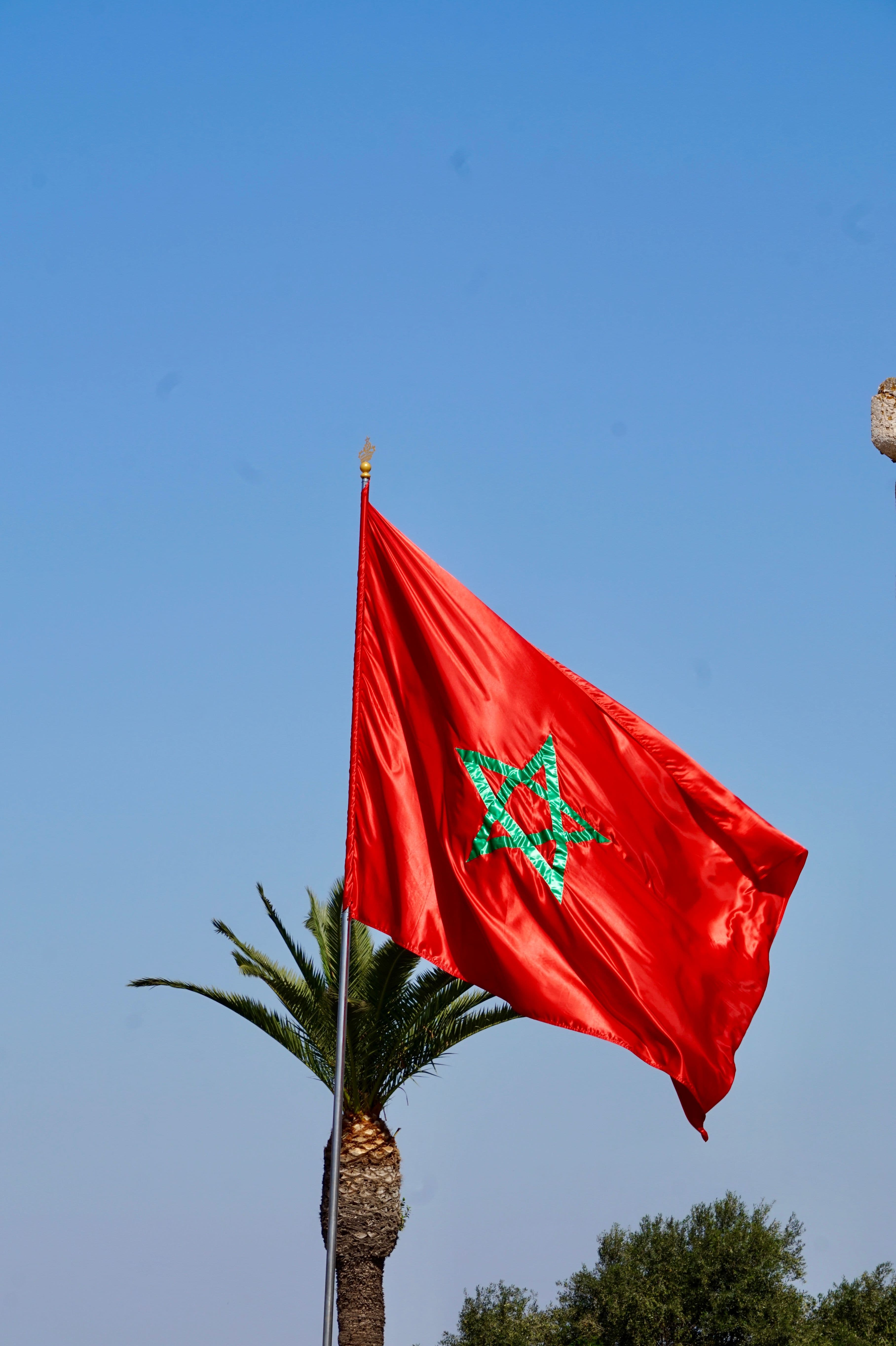 The flag of Morocco, red with a green pentagram, waves against a clear blue sky.