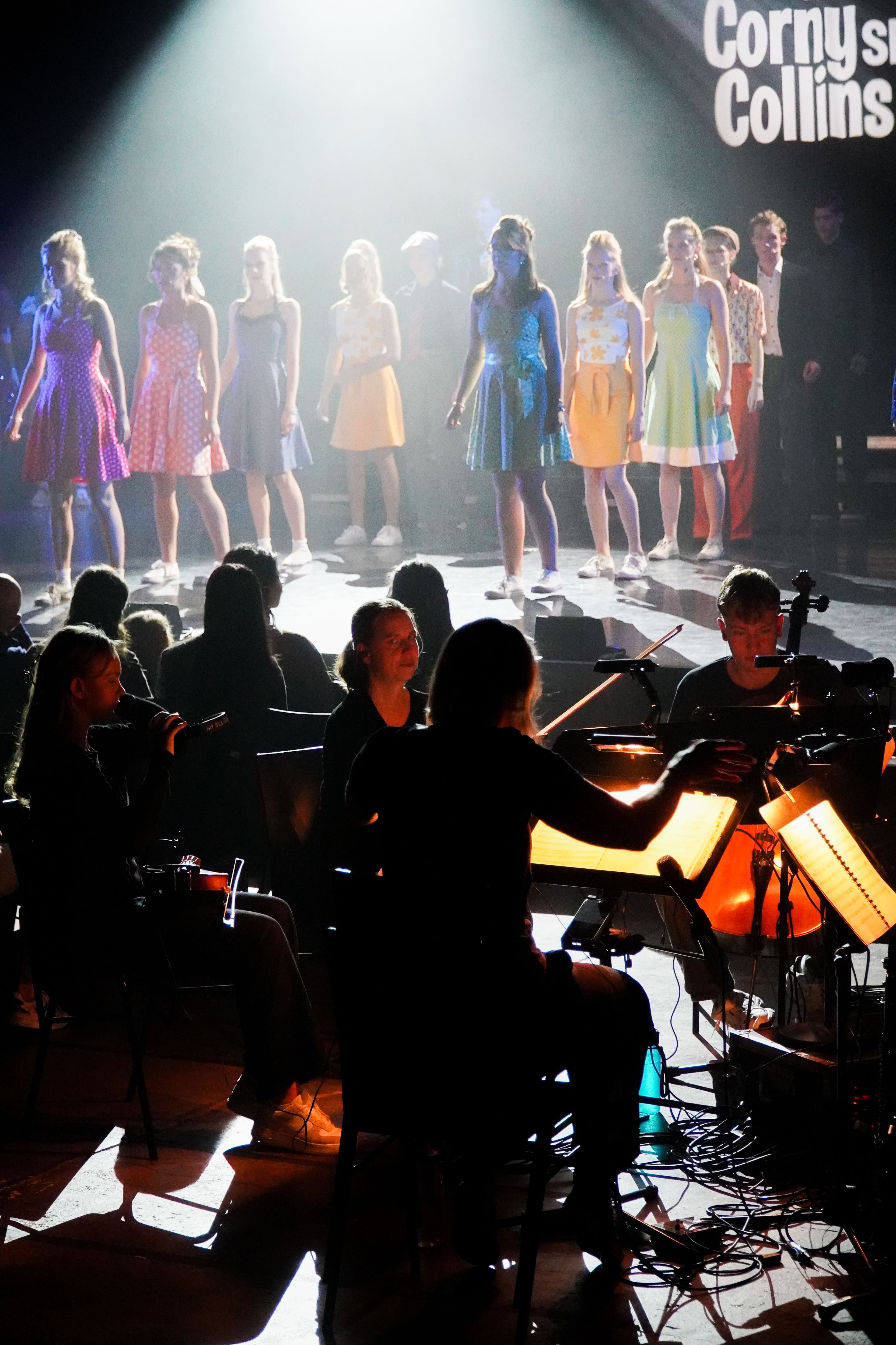 Im Vordergrund eine Band mit Dirigentin, im Hintergrund Schauspieler auf einer Bühne.