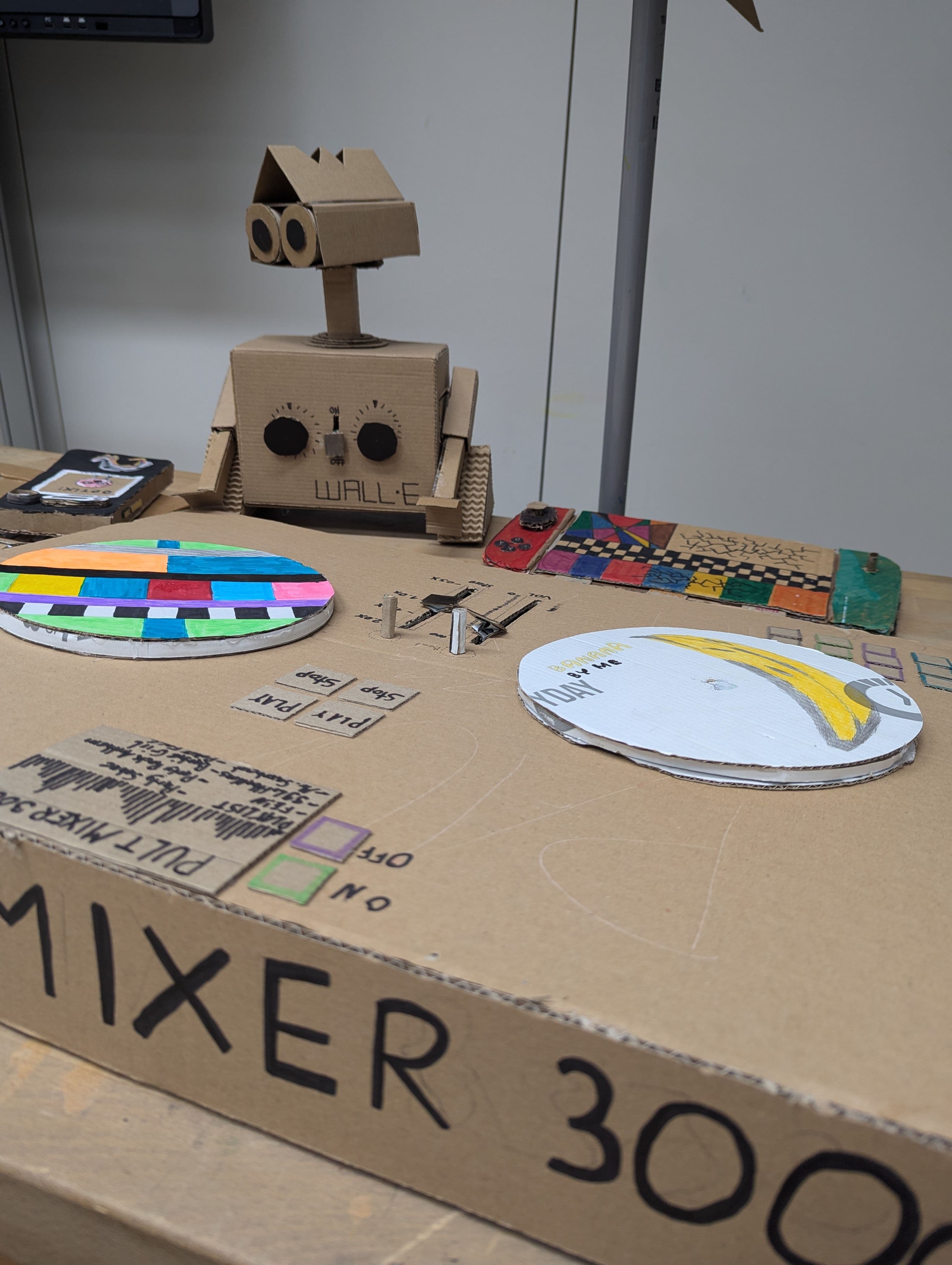 Papp-DJ-Pülz mit Papproboter im Hintergrund