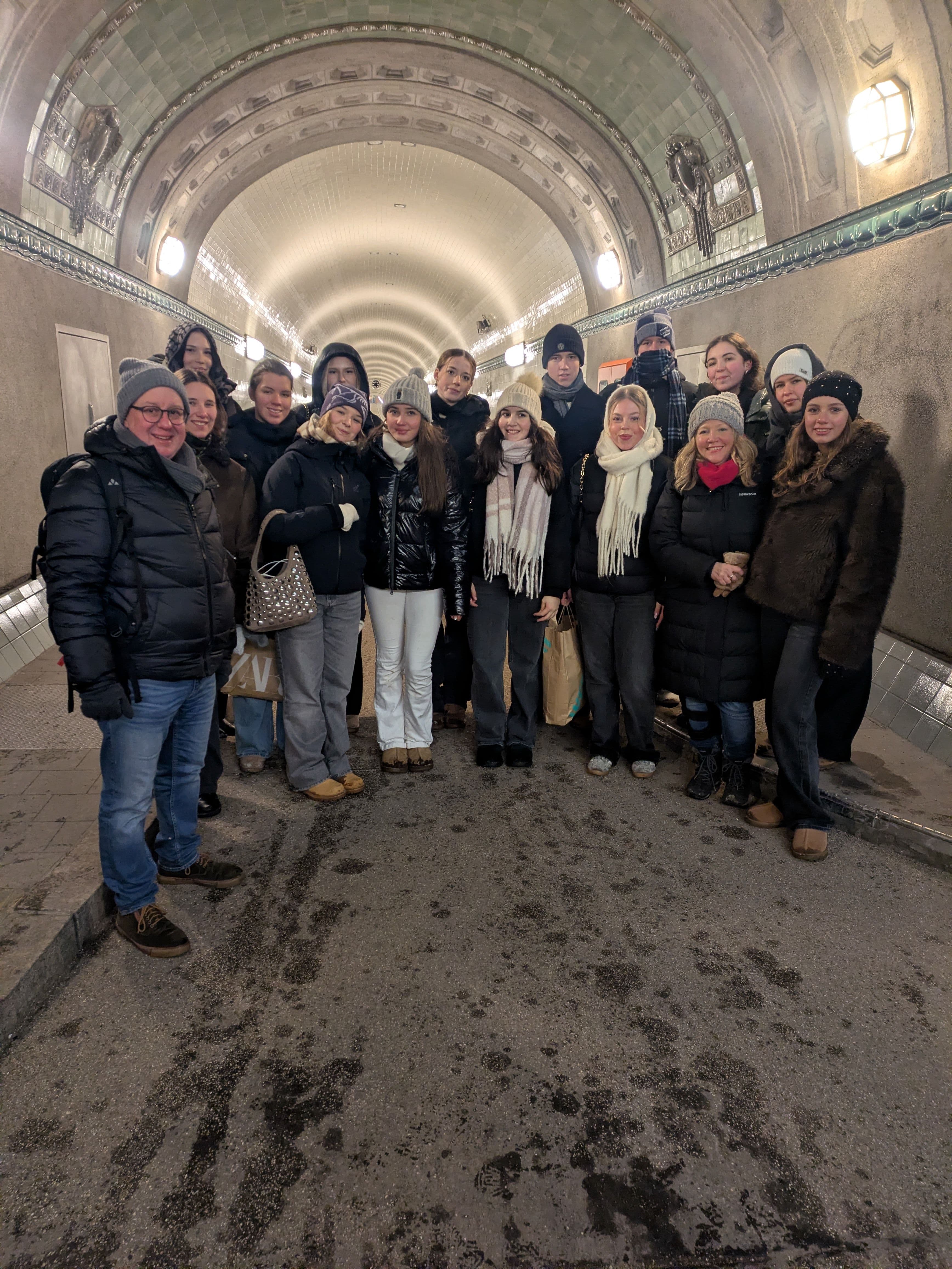 A group of people in winter clothing stands inside a well-lit, arched tunnel.