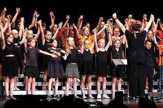 a large group of children are standing on a stage with their hands in the air .