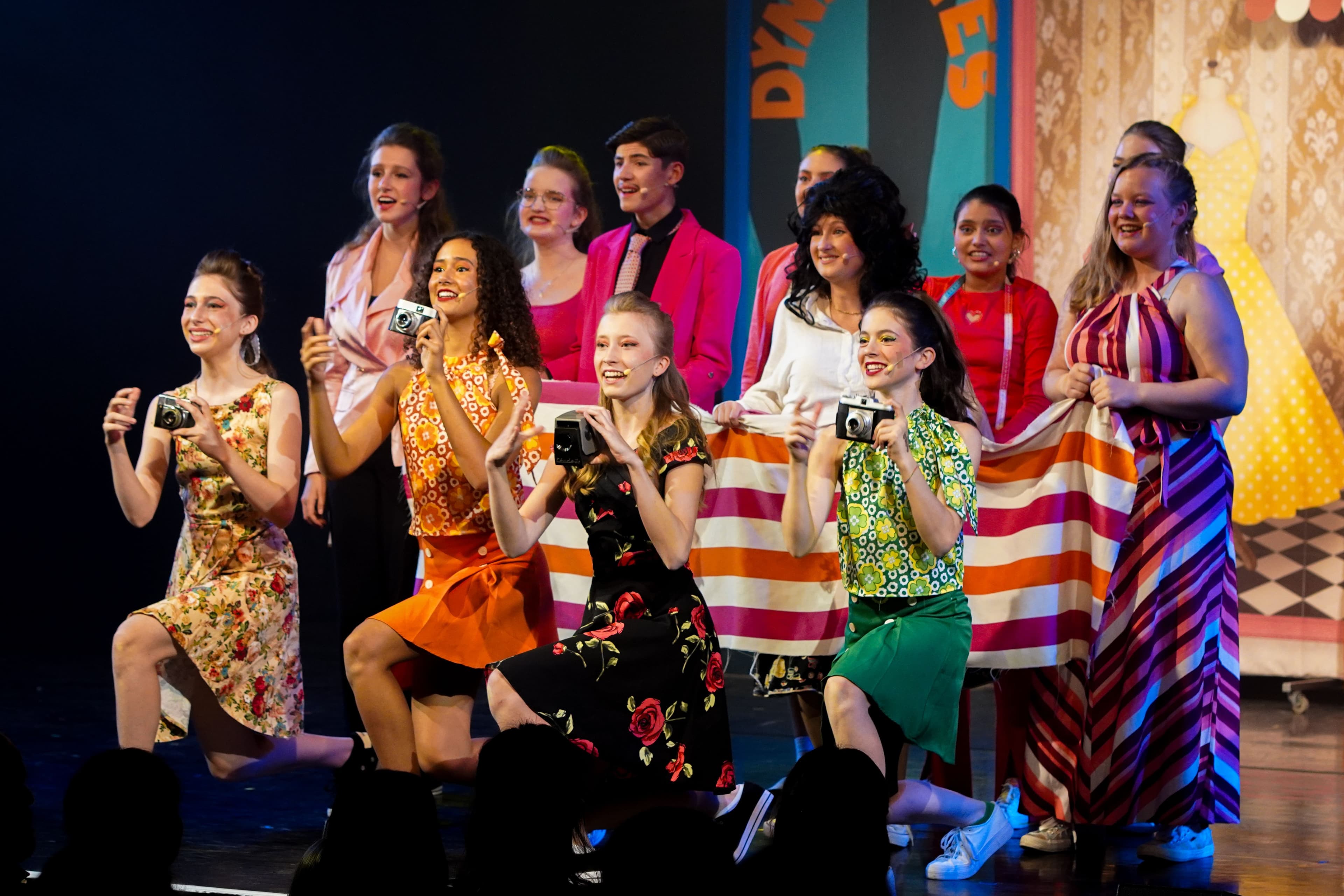 Schauspieler mit Kameras im Vordergrund, Schauspieler mit bunten Stoffen im Hintergrund.