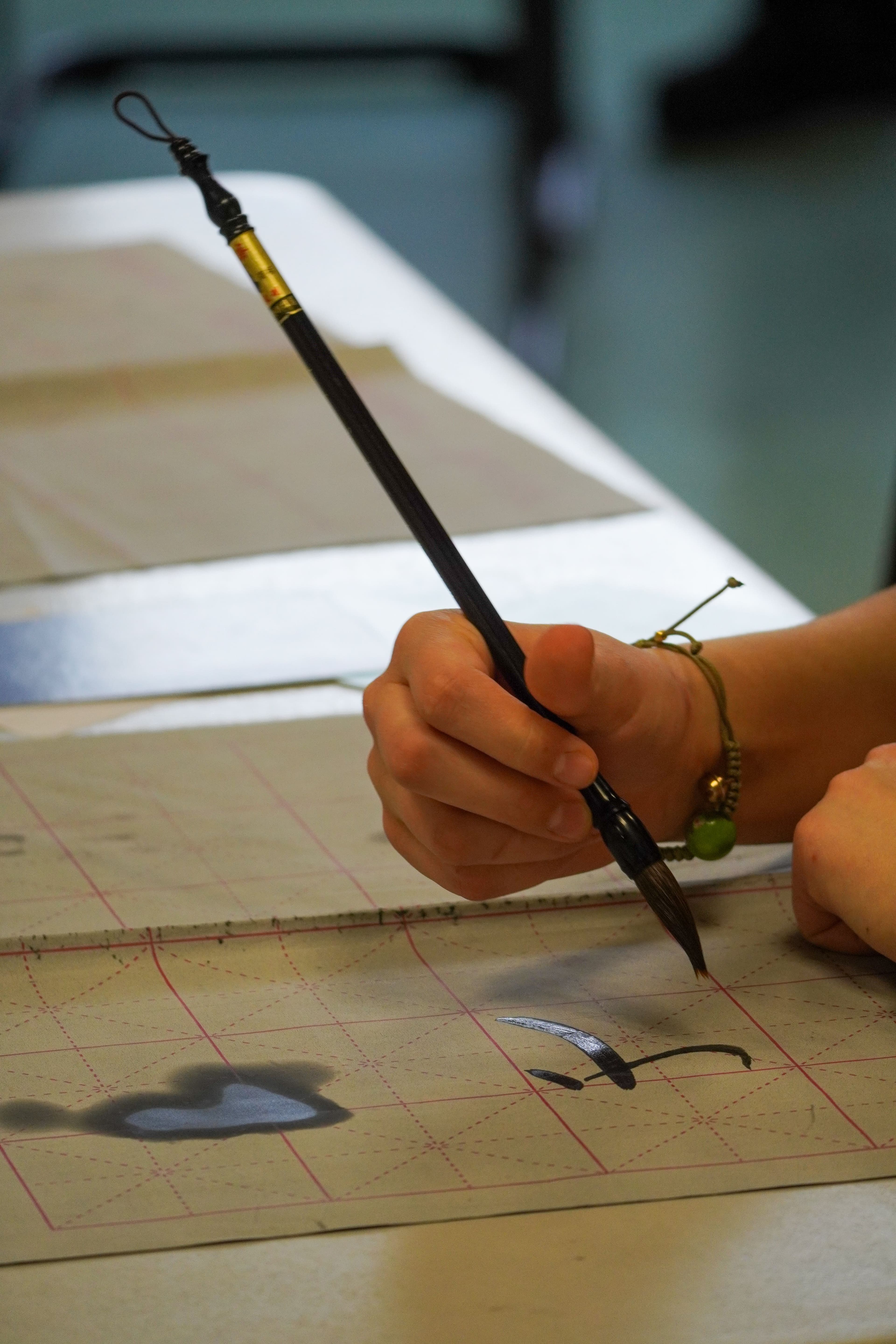 Chinesischer Pinsel in einer Hand beim Malen von Schriftzeichen.