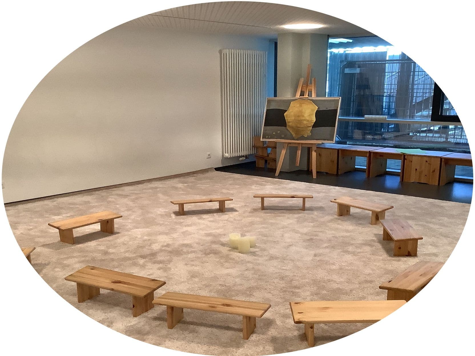 a circle of wooden benches in a room with a painting on an easel .